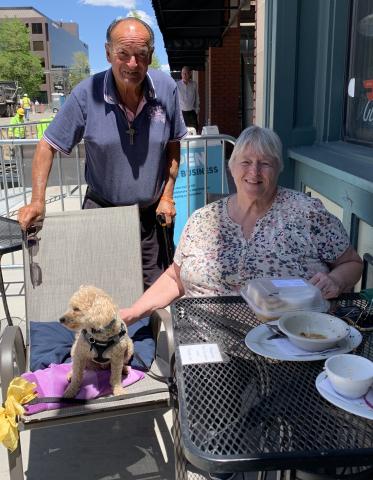 Two patrons of an eatery on Tejon Street smiling for a photo with their dog. They are sitting outside of the restaurant.