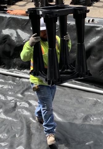 A worker carries a plastic tree cell to be placed in the ground.