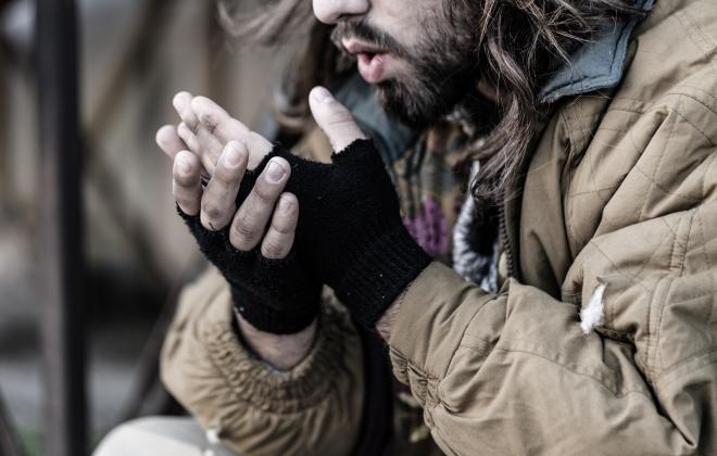 A homeless person warming their hands with their breath